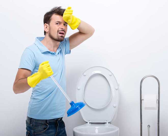 man unclogging his toilet with a plunger